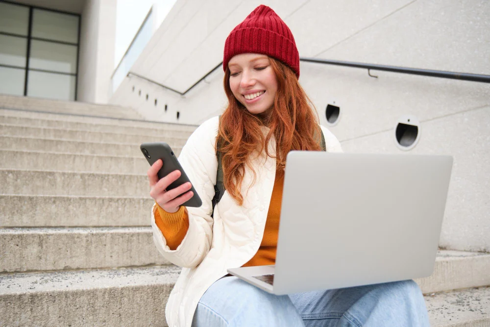 Dziewczyna wykorzystuje internet mobilny w telefonie, aby podłączyć do sieci laptop.